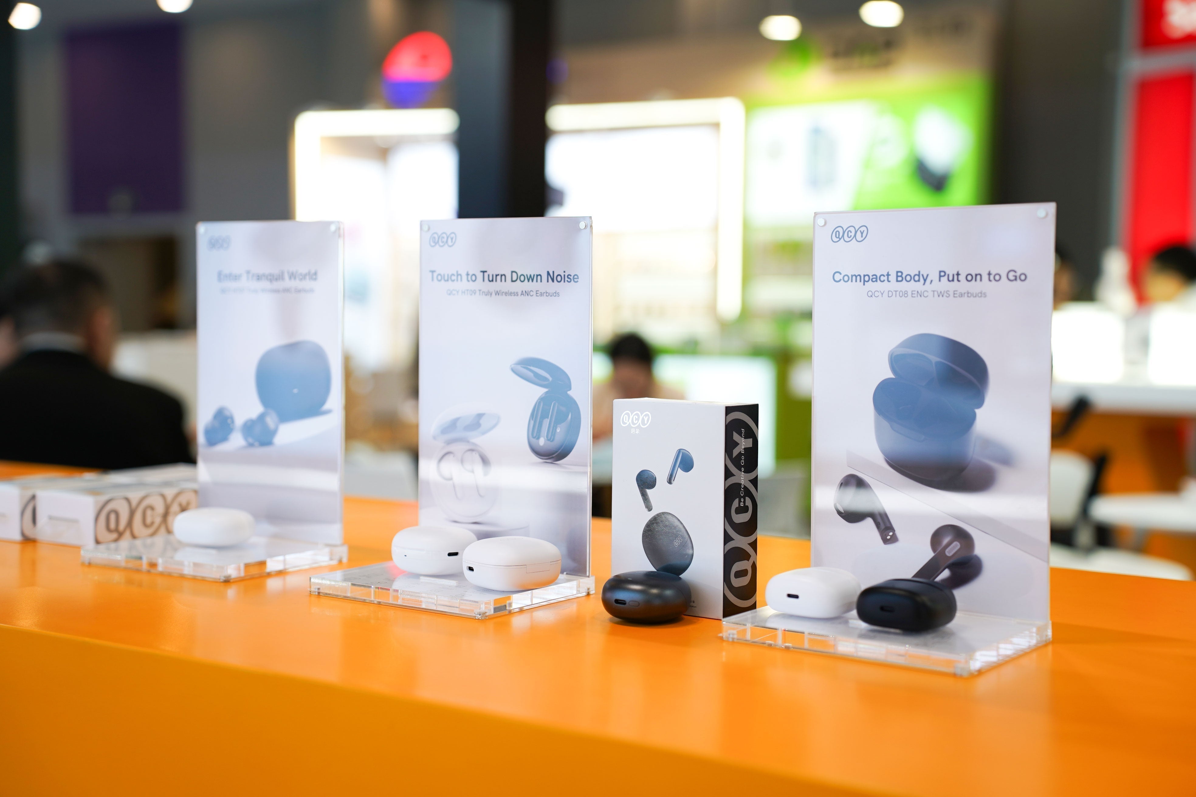 QCY Bluetooth-Kopfhörer auf orangem Tisch: Modelle mit ANC, Touch-Steuerung & kompakter Bauart im Vergleich.