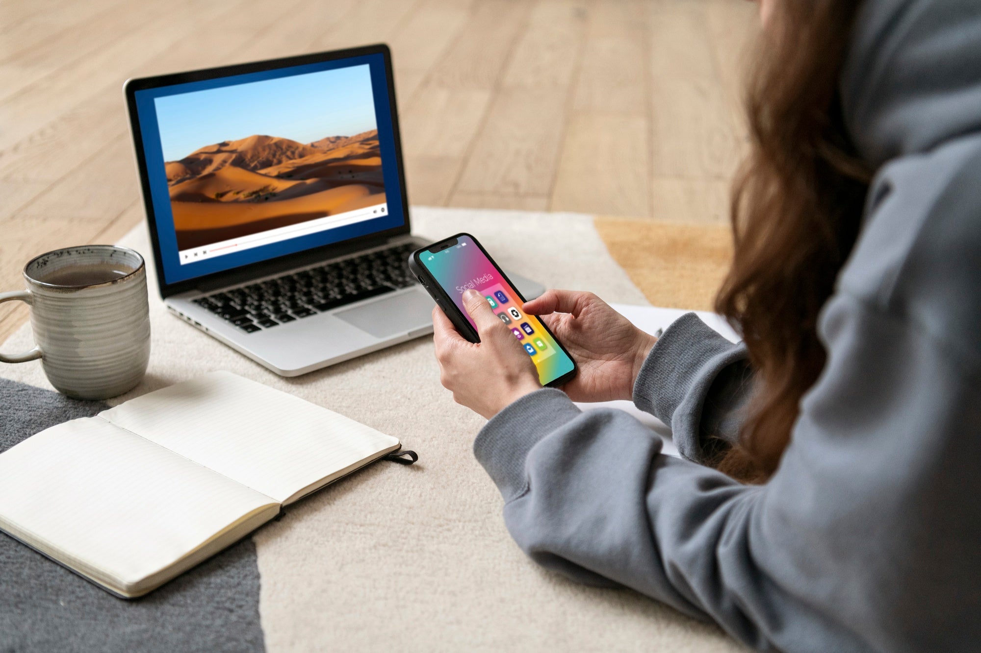 Frau nutzt Smartphone und Laptop für Firmware-Update der Kopfhörer – Optimierung der Leistung im Home-Office.