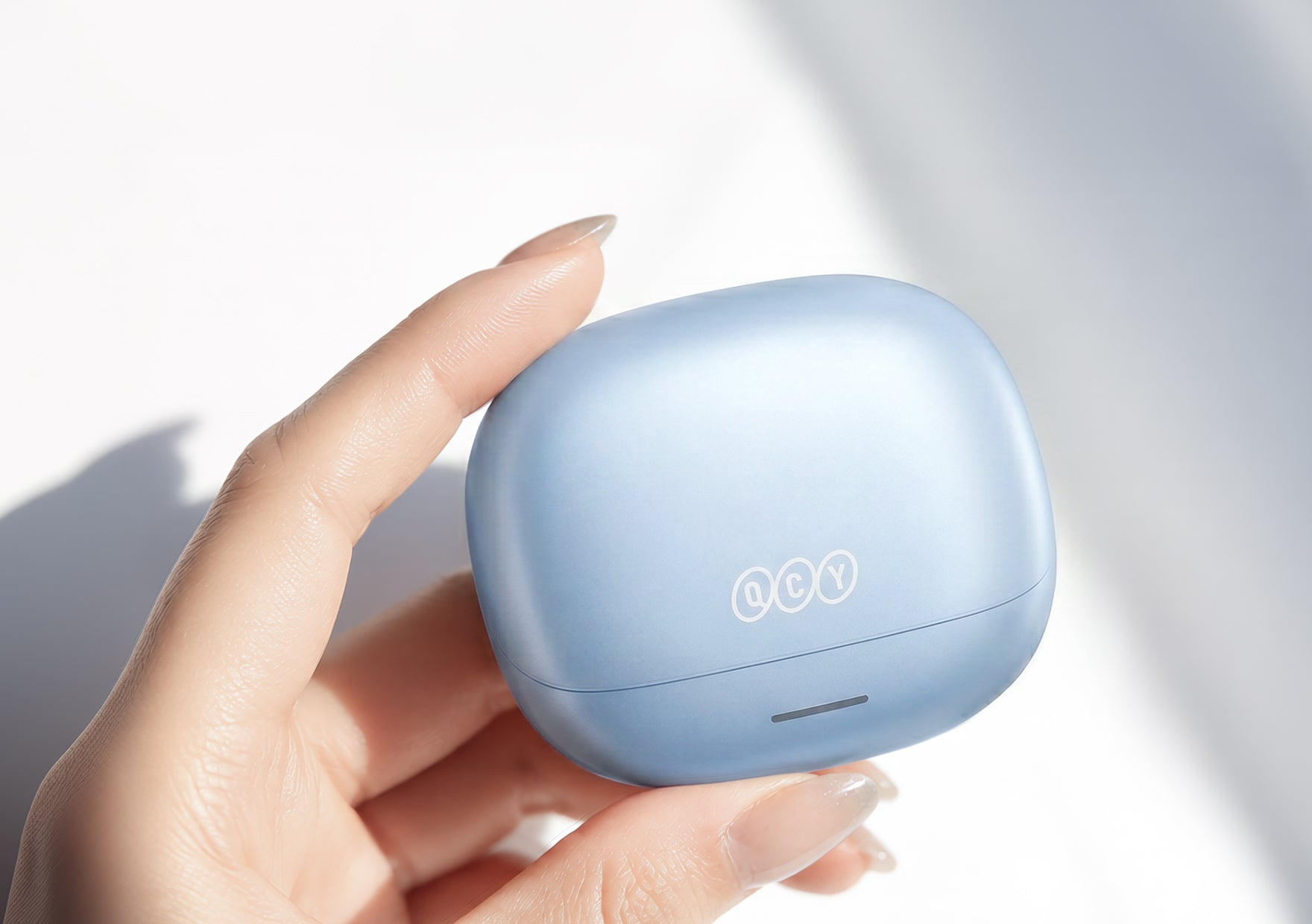 QCY Bluetooth-Kopfhörer in hellblau, im Ladecase gehalten.