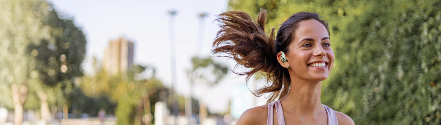 Lächelnde Frau mit Haar in Wind, die In-Ear-Kopfhörer trägt – Sport & Musik im Freien.