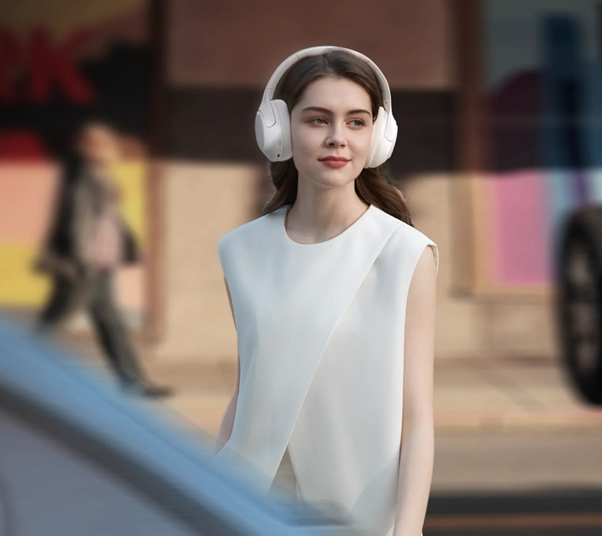 Frau mit weißen Over-Ear-Kopfhörern im urbanen Umfeld, stilvolle Mode, moderne Technologie