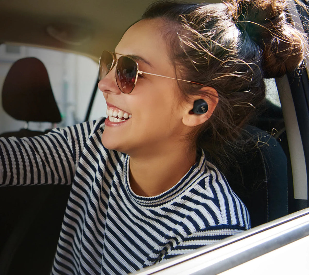 Frau mit Sonnenbrille und kabellosen Ohrhörern im Auto