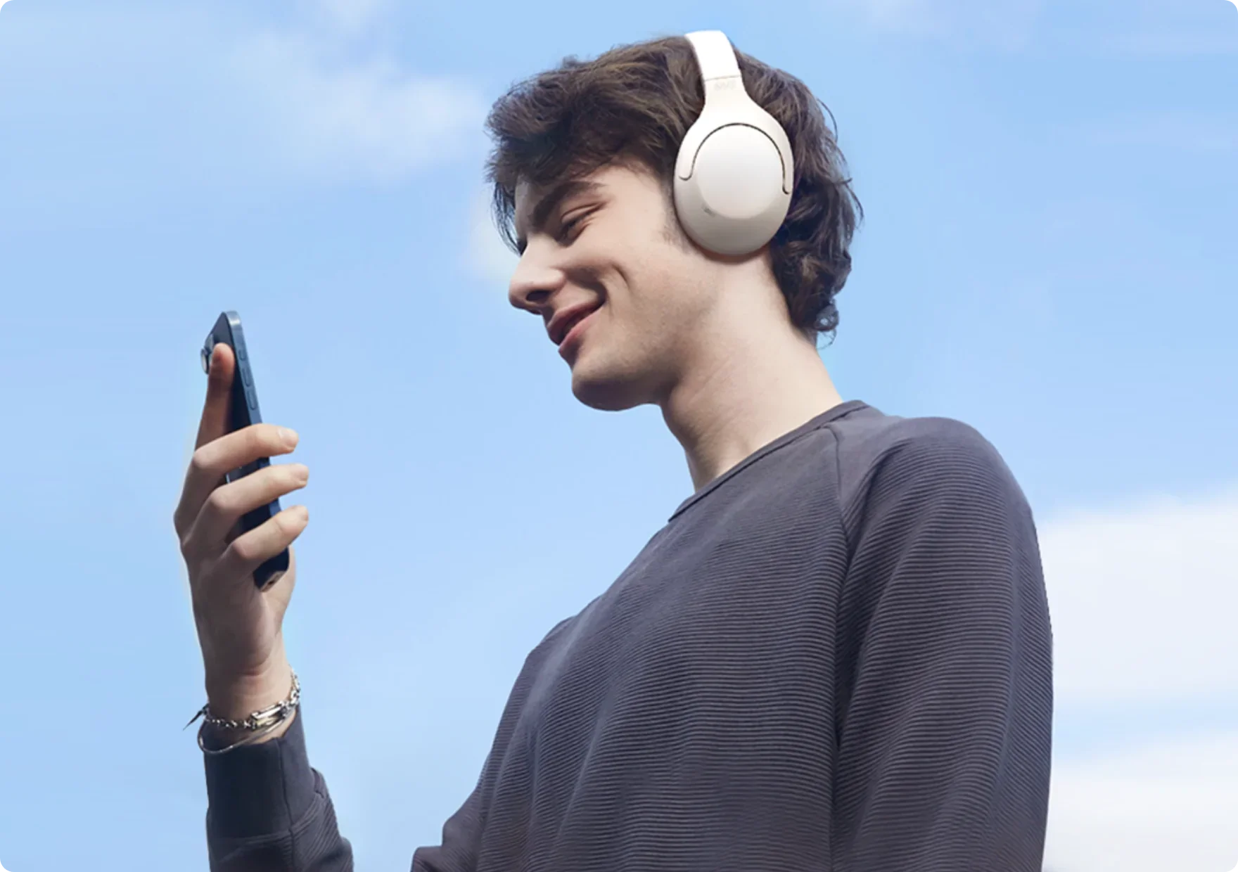 Junge Mann mit weißen Kopfhörern und Smartphone unter blauem Himmel.