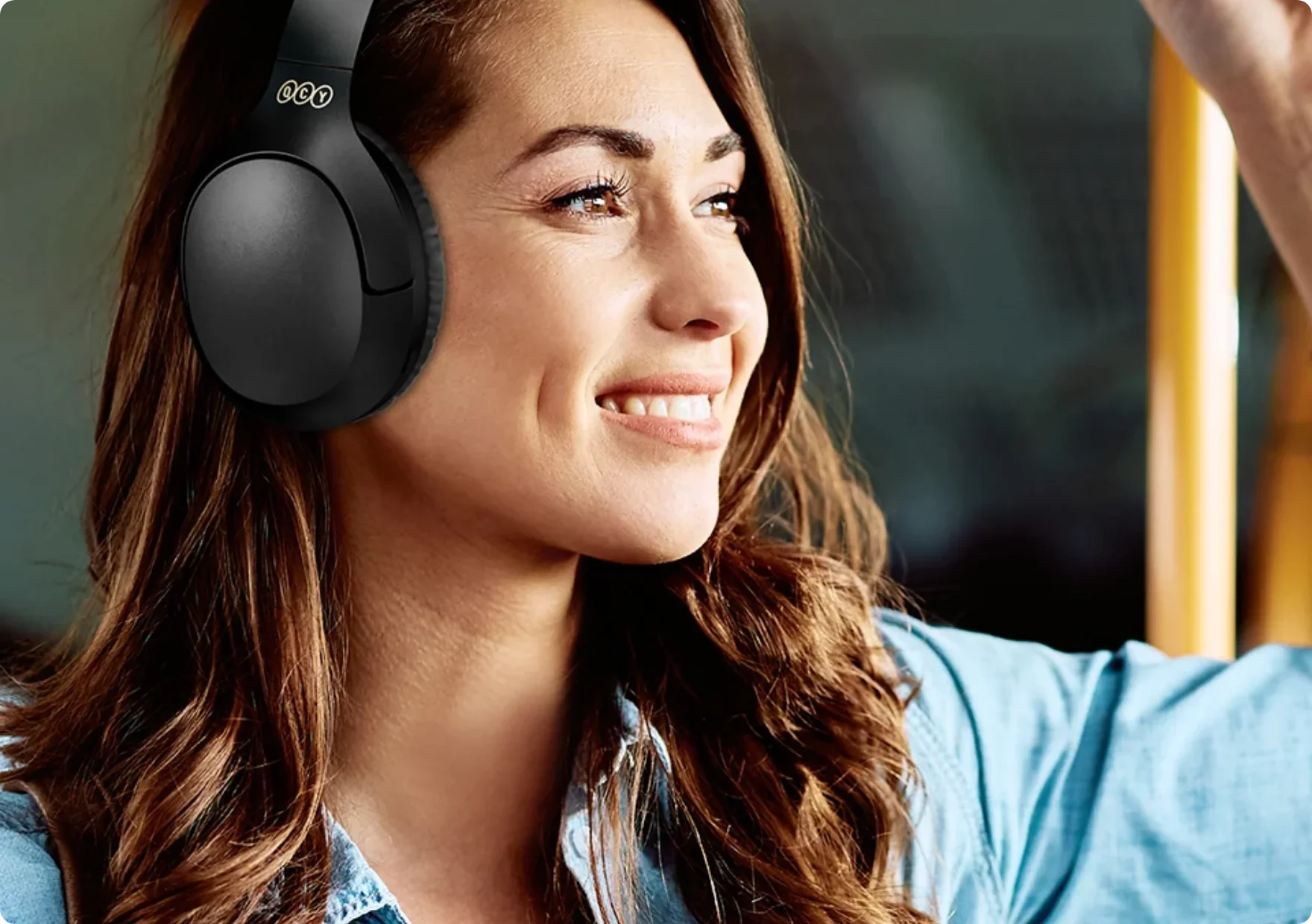 Frau mit schwarzen Over-Ear-Kopfhörern lächelnd im Bus.