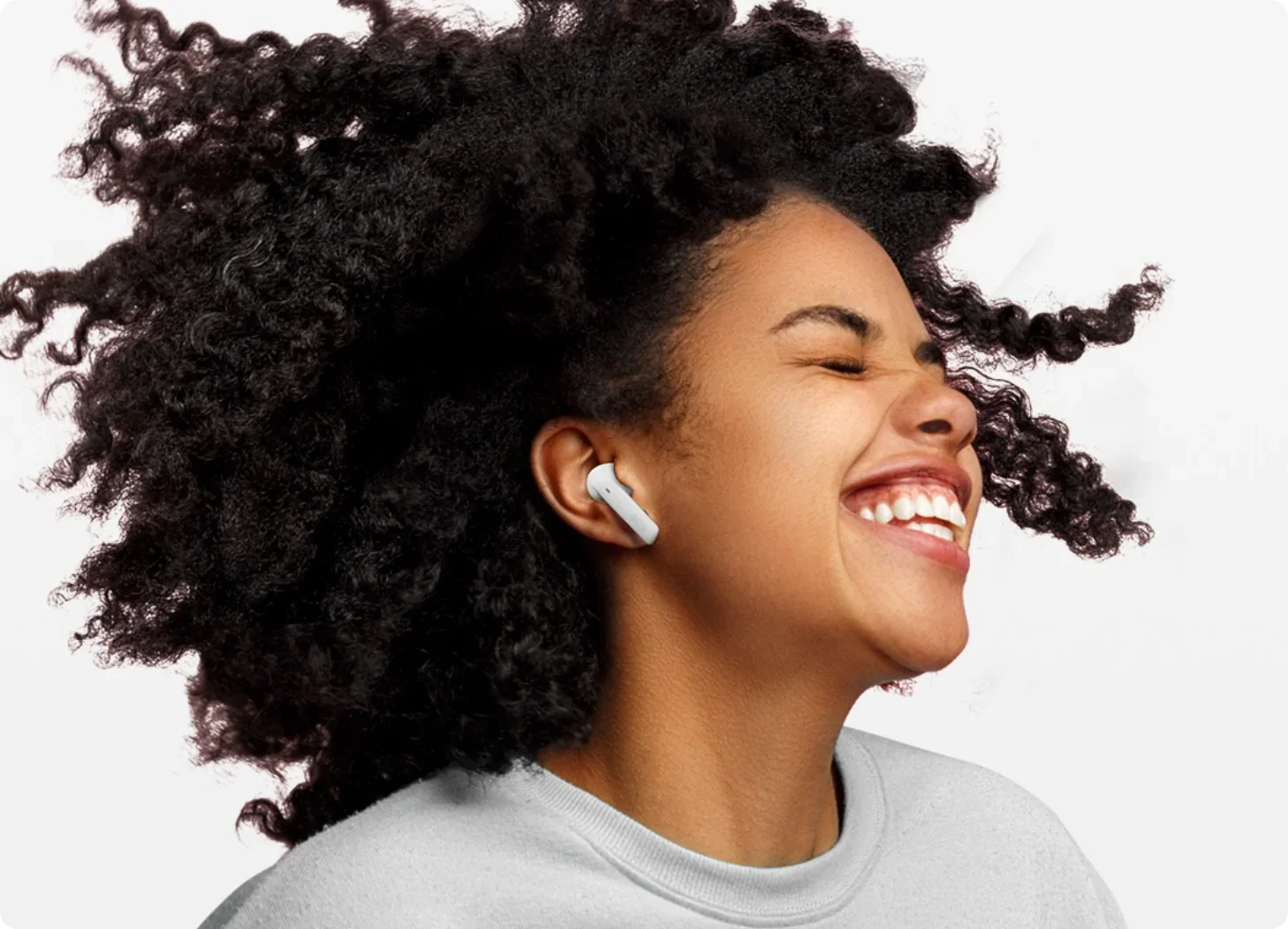 Glückliche Frau mit lockigem Haar und weißen In-Ear-Kopfhörern.