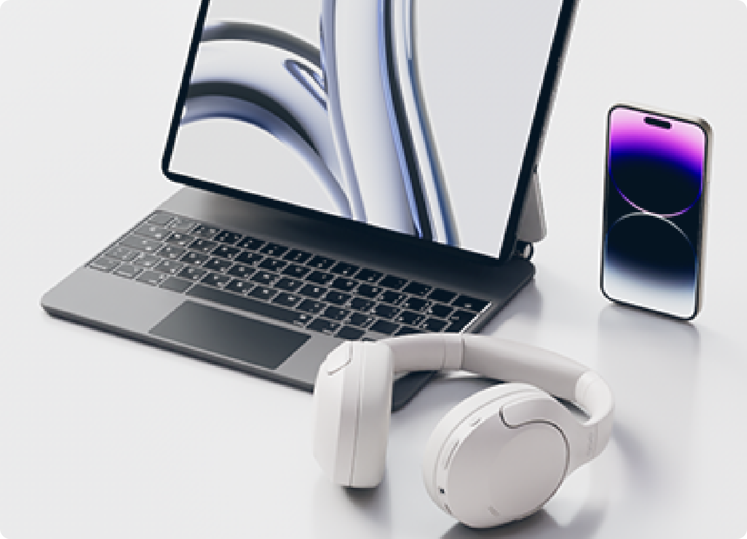 Modernes Laptop-Set mit weißem Headset und Smartphone auf hellem Tisch.