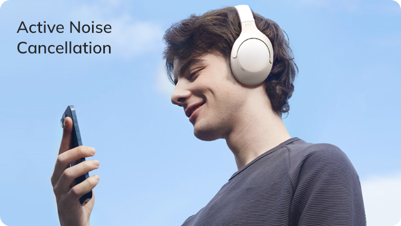 Junger Mann mit weißen ANC-Kopfhörern, lächelnd beim Musikhören unter blauem Himmel – Active Noise Cancellation im Freien erl