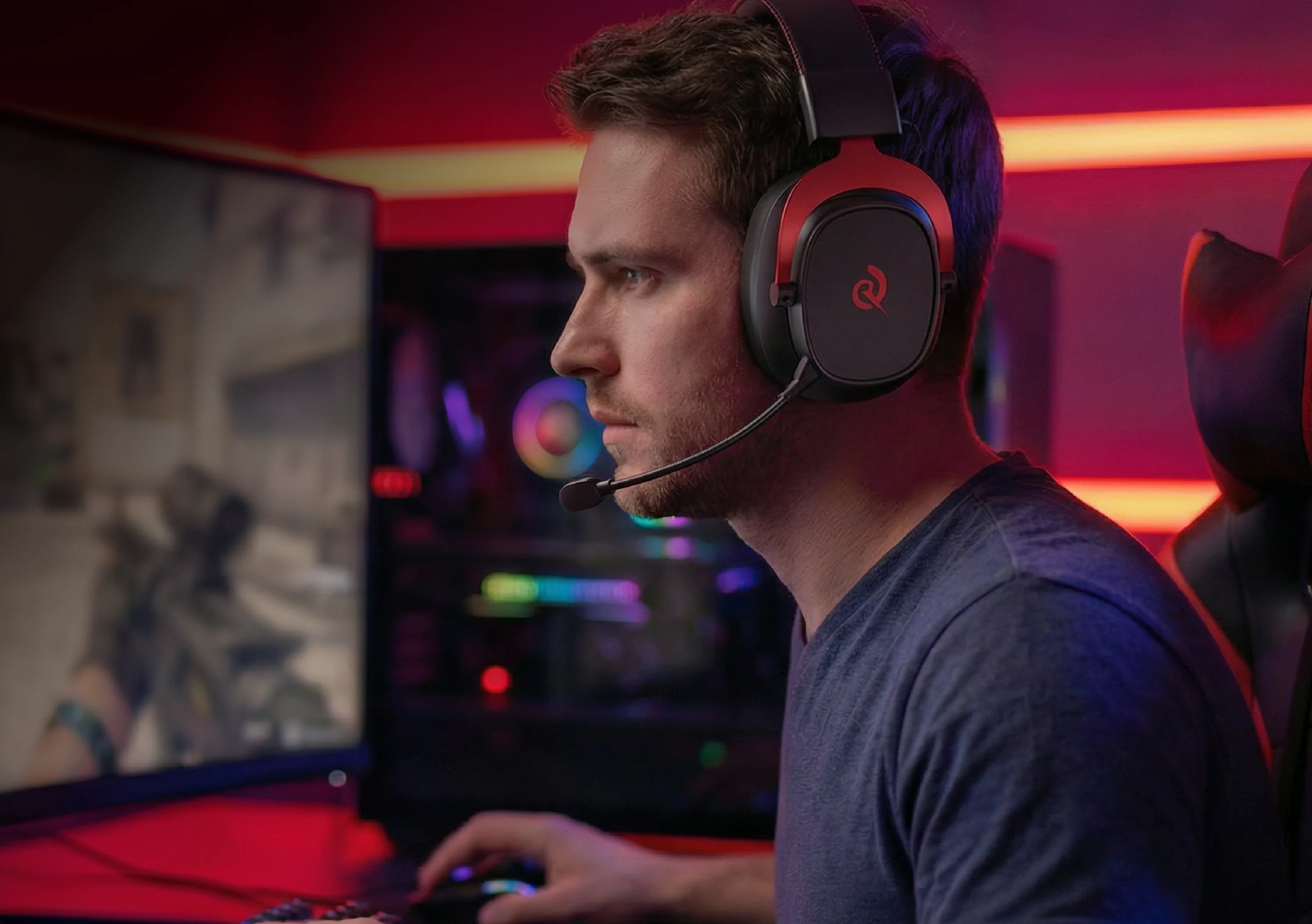 Mann mit Gaming-Headset und Mikrofon vor PC-Monitor, leuchtende RGB-Beleuchtung im Hintergrund