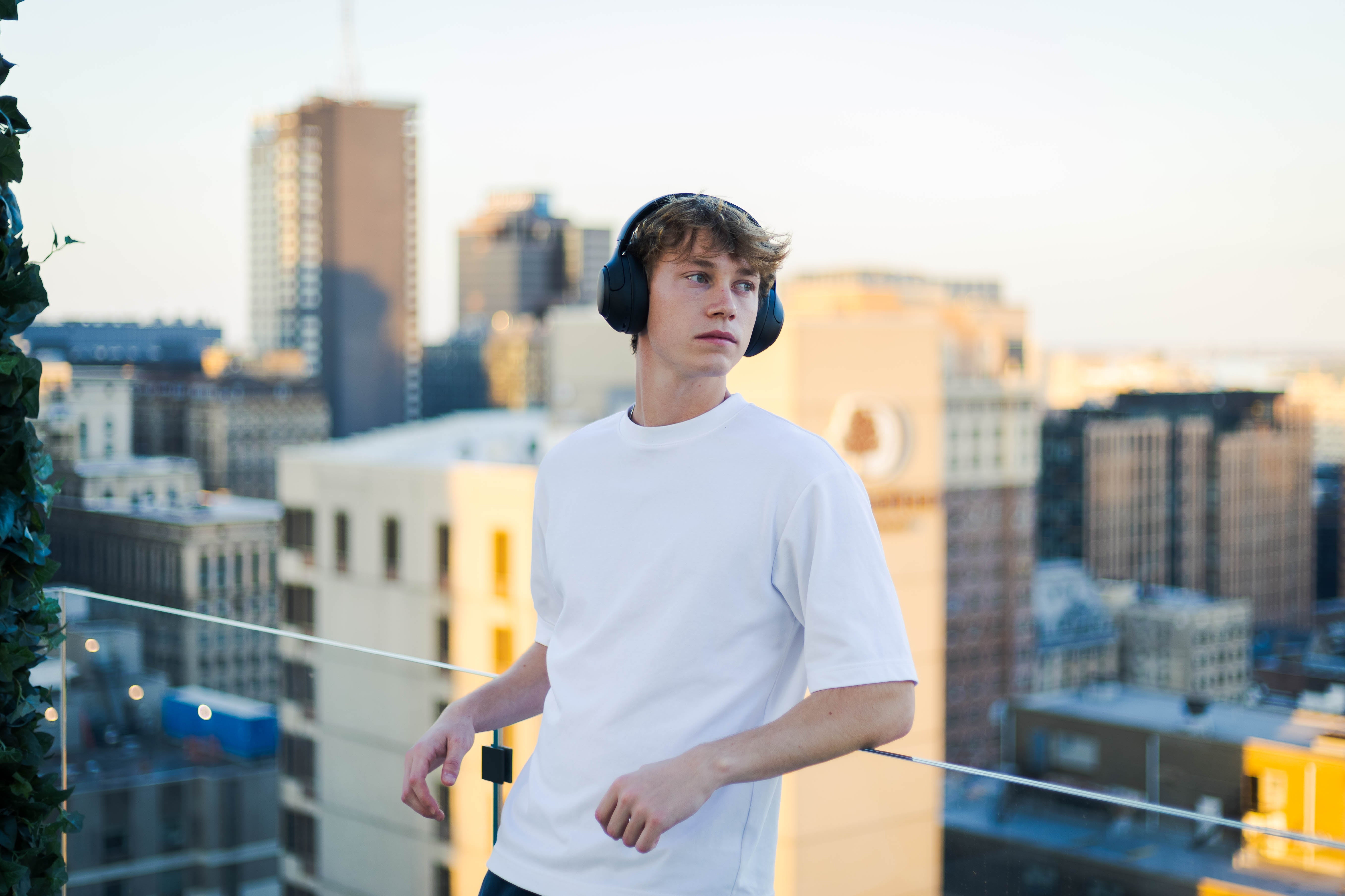 Junger Mann mit Kopfhörern auf Dachterrasse vor Stadtblick