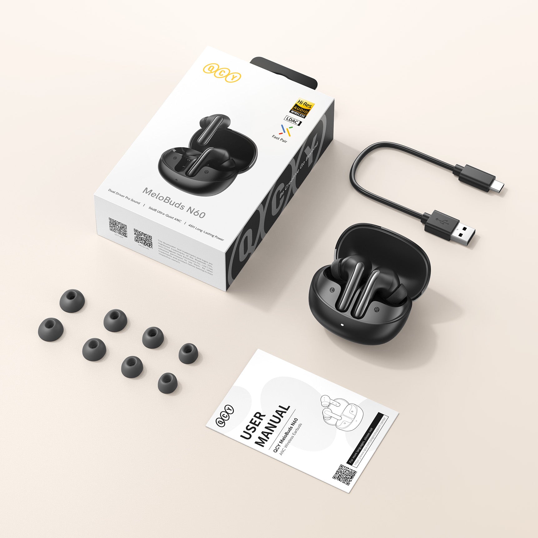 QCY MeloBuds N60 Kabellose Ohrhörer mit Ladecase, USB-Kabel, Ersatz-Ohrstöpseln und Bedienungsanleitung auf hellem Hintergrun